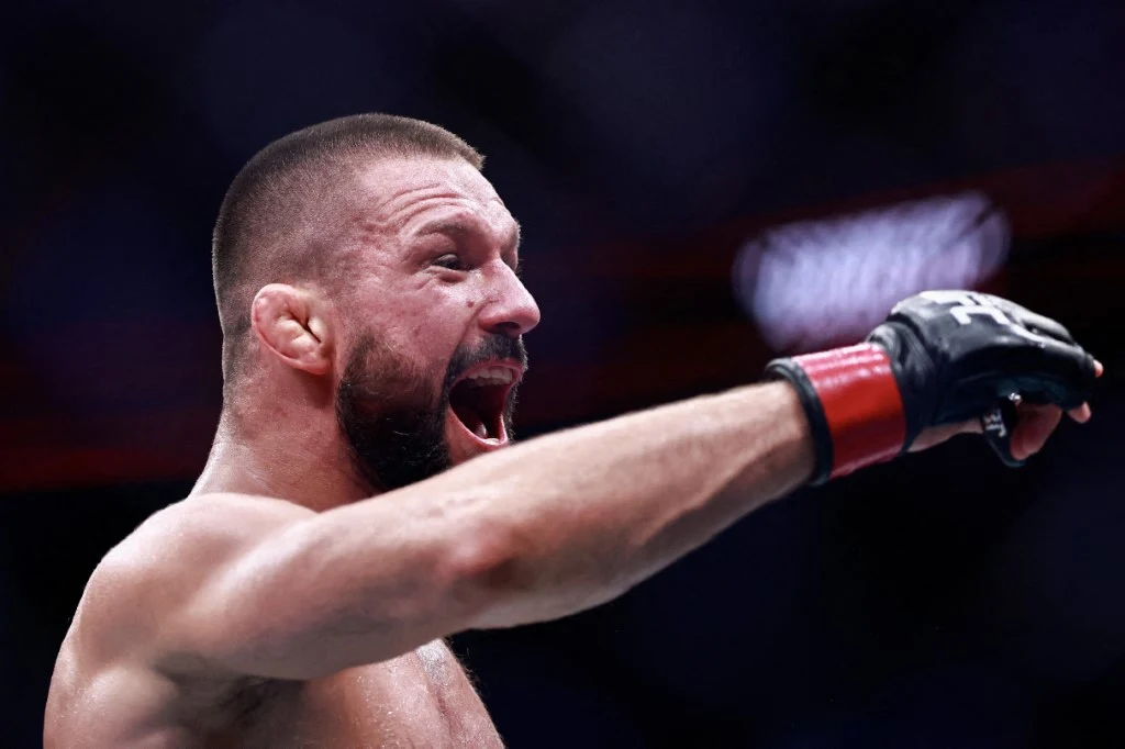 Mateusz Gamrot stoczył 13 walk dla UFC Zawodnik MMA z krótkimi włosami i brodą w sportowych rękawicach energicznie gestykuluje podczas walki na ringu.