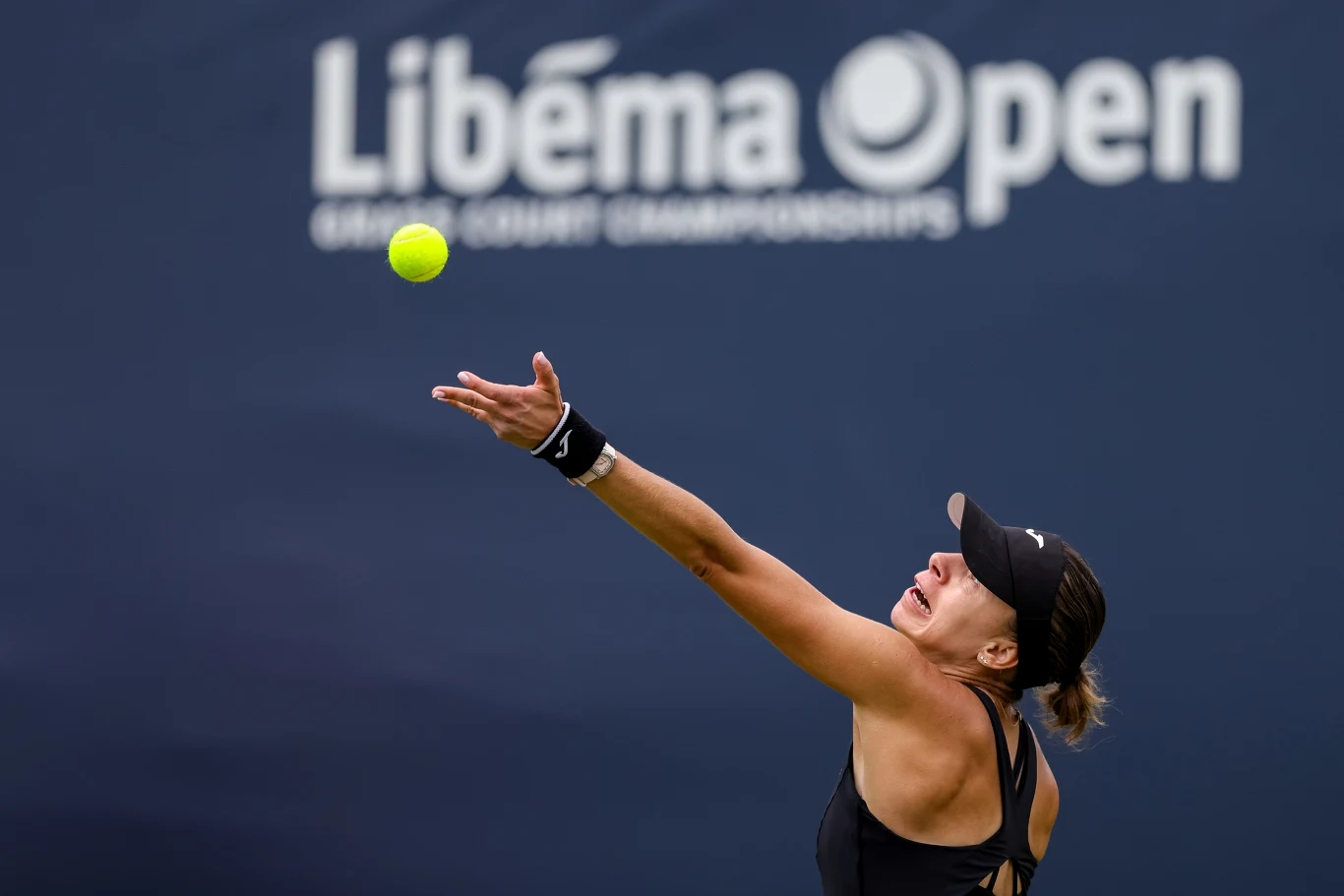 Magda Linette Zawodniczka w czarnym stroju przygotowująca się do serwisu podczas turnieju tenisowego Libéma Open, z żółtą piłką unoszącą się w powietrzu.