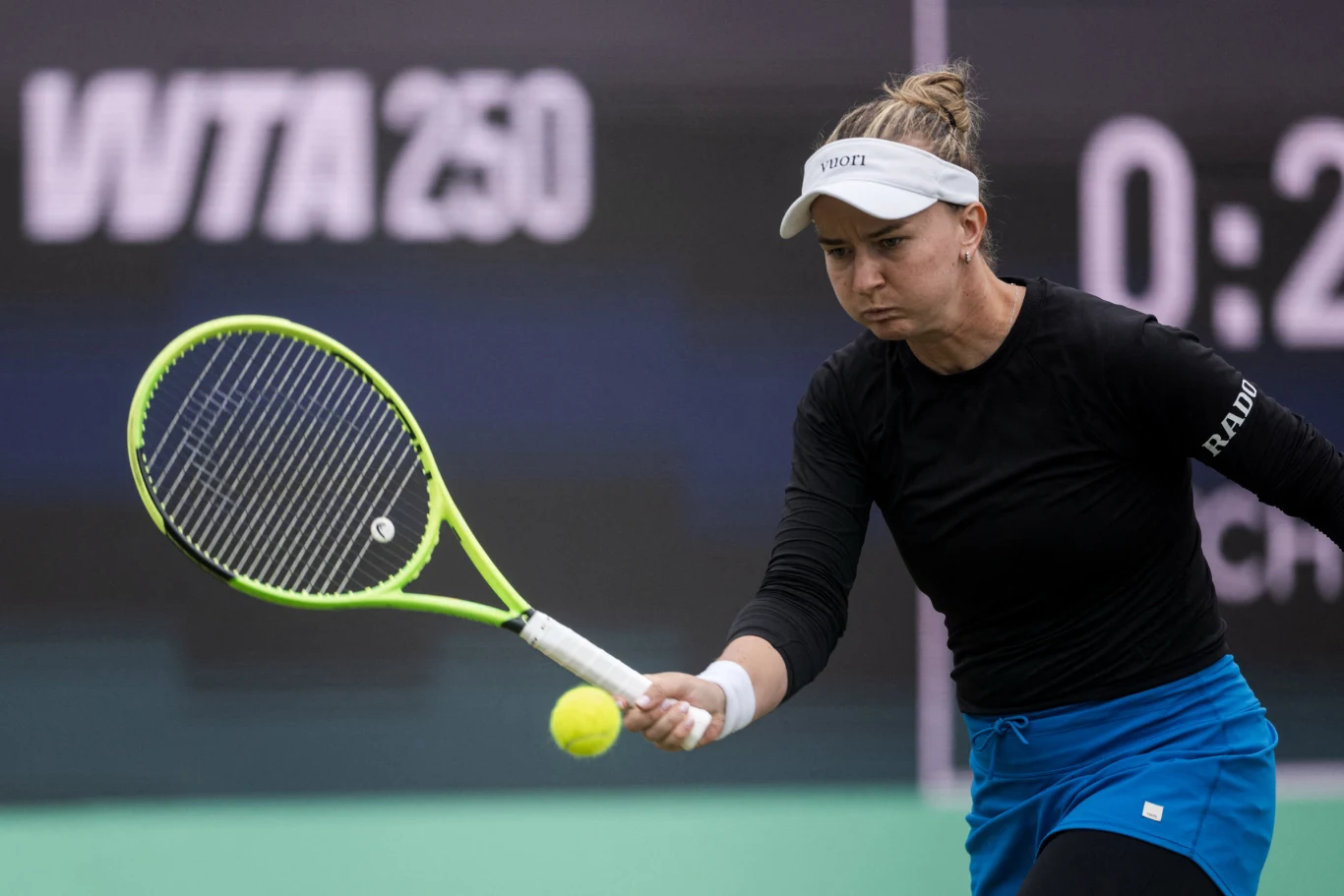 Barbora Krejcikova Tenisistka w czarnej koszulce i niebieskiej spódniczce odbija żółtą piłkę rakietą na tle tablicy z napisem WTA 250.