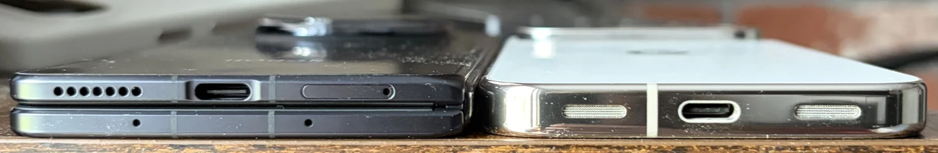 Dwa smartfony ustawione obok siebie na płaskiej powierzchni, widoczne z perspektywy dolnej krawędzi; po lewej czarny telefon z portem USB-C, kratką głośnika i otworem na kartę SIM, po prawej biały telefon z portem USB-C i otworami głośników po obu stro...
