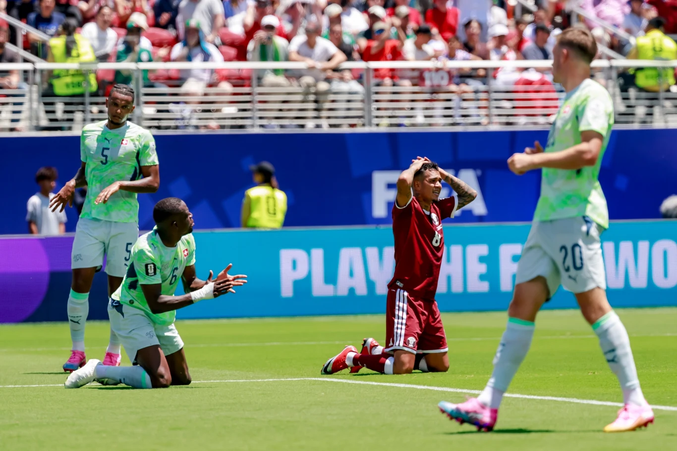 Szwajcaria - Katar w mundialu 2026 Piłkarze dwóch drużyn reagują emocjonalnie na boisku podczas meczu, dwaj zawodnicy w zielonych strojach klęczą z wyciągniętymi rękami, a zawodnik w bordowym stroju trzyma głowę w geście rozczarowania.