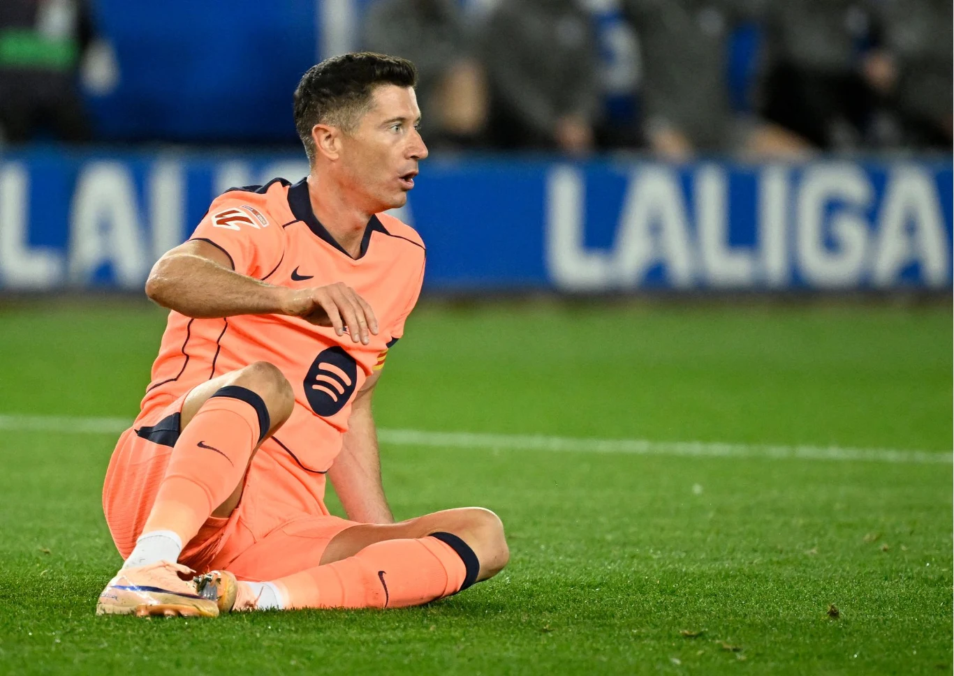 Piłkarz w pomarańczowym stroju z logiem Spotify siedzi na murawie boiska, z wyrazem zaskoczenia na twarzy, w tle widoczny fragment napisu LaLiga.