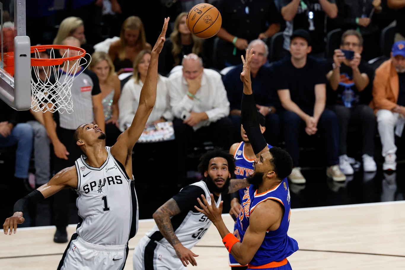 Kadr z meczu Knicks - Spurs Koszykarz San Antonio Spurs blokujący rzut zawodnika New York Knicks podczas meczu, piłka przelatuje nad wyciągniętymi ramionami obu graczy.