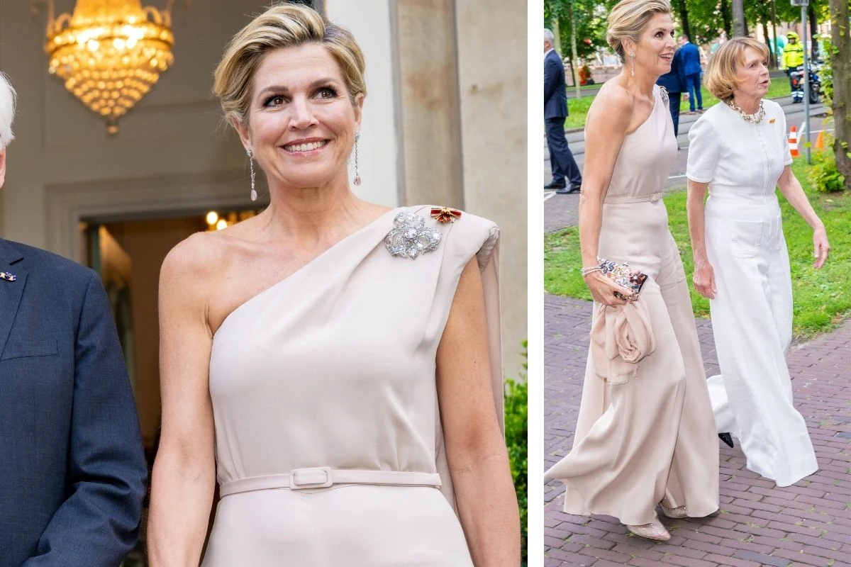 Elegancko ubrana kobieta w jasnej, długiej sukni na jedno ramię, z ozdobą na ramieniu, podczas oficjalnego wyjścia w towarzystwie innej kobiety w białej kreacji.