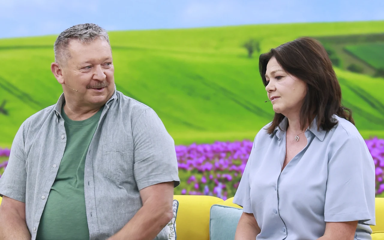 Wiesław i Barbara Nowobilscy w "halo tu polsat" Dwie osoby siedzące na żółtej kanapie, rozmawiające ze sobą na tle zielonego, pagórkowatego krajobrazu z fioletowym pasem kwiatów.