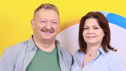 Dwie uśmiechnięte osoby stojące obok siebie na tle żółtej ściany z kolorowym, abstrakcyjnym wzorem.