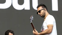 Dwóch muzyków podczas występu na scenie, jeden z nich gra na gitarze elektrycznej, drugi stoi obok skoncentrowany na instrumencie klawiszowym.