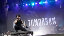 Wokalista z mikrofonem przykuca na podwyższeniu na scenie podczas koncertu, w tle widoczny duży napis 'Bury Tomorrow' oraz członkowie zespołu przy swoich instrumentach.