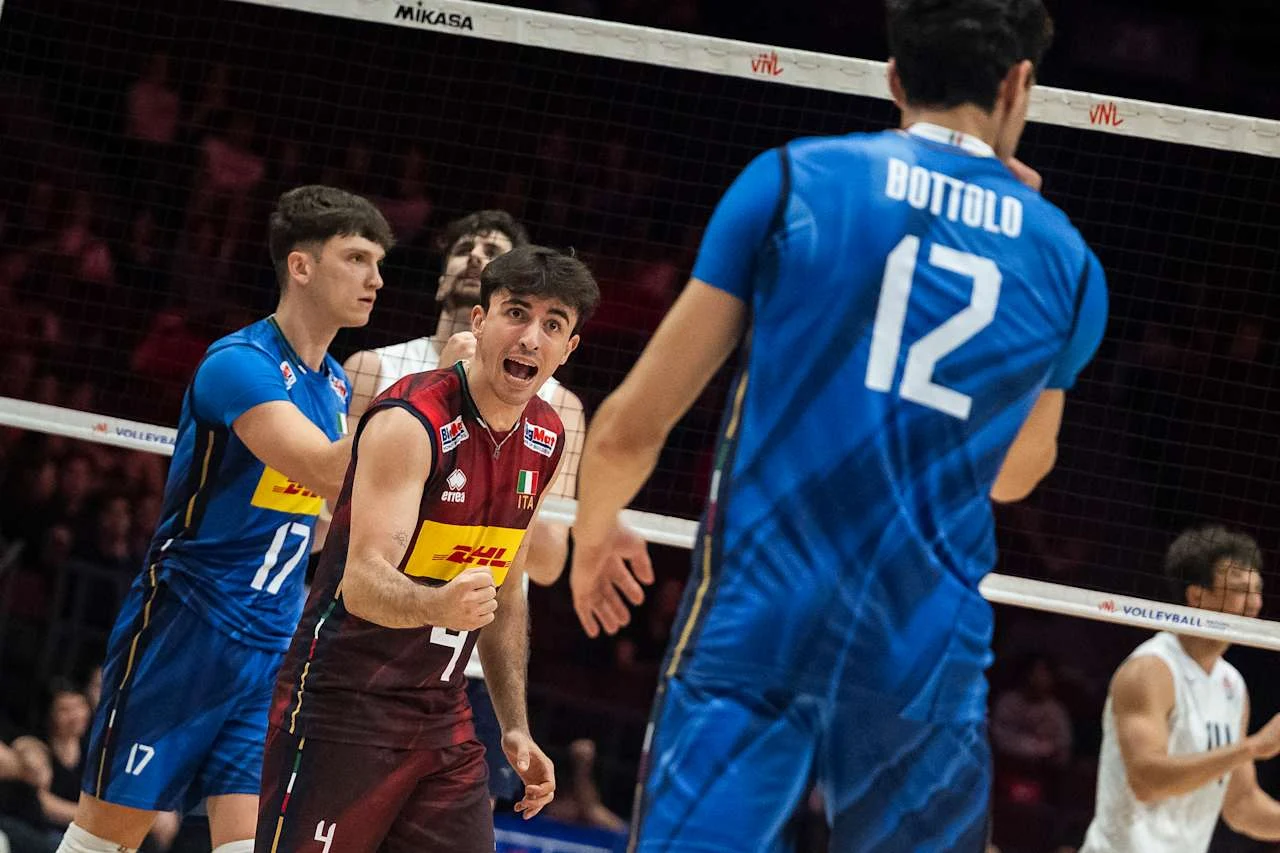 Zawodnik w bordowym stroju dynamicznie reaguje po zdobyciu punktu podczas meczu siatkówki, naprzeciwko graczy w niebieskich strojach z numerami 12 i 17.