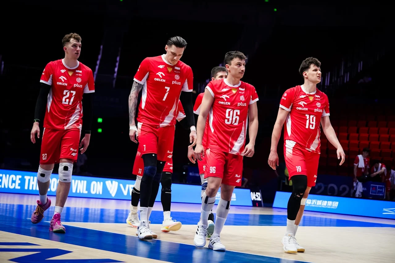 Grupa siatkarzy w czerwonych strojach reprezentacyjnych idzie razem po boisku sportowym, wyróżniają się numery 27, 7, 96 i 19 na koszulkach.