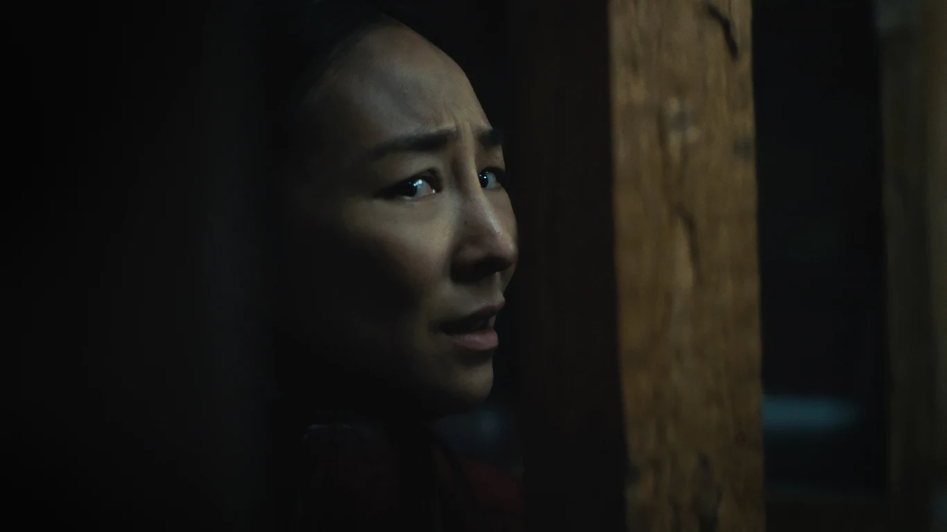 Greta Lee w filmie "Ostatni dom" Twarz kobiety z wyraźnym wyrazem niepokoju ukryta częściowo za drewnianym elementem.