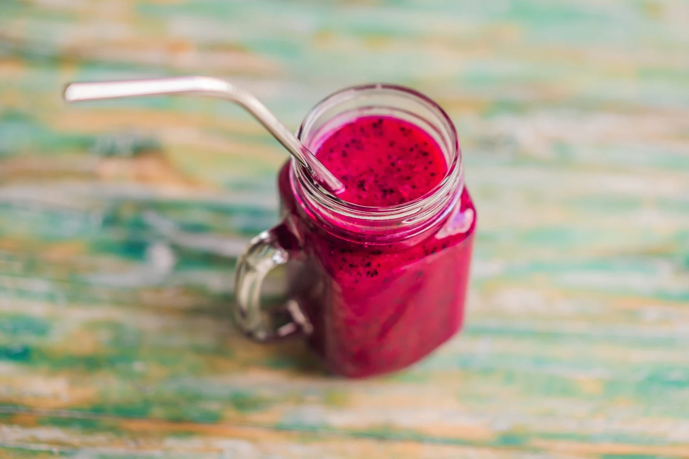 Szklany słoik z różowym smoothie i metalową słomką.