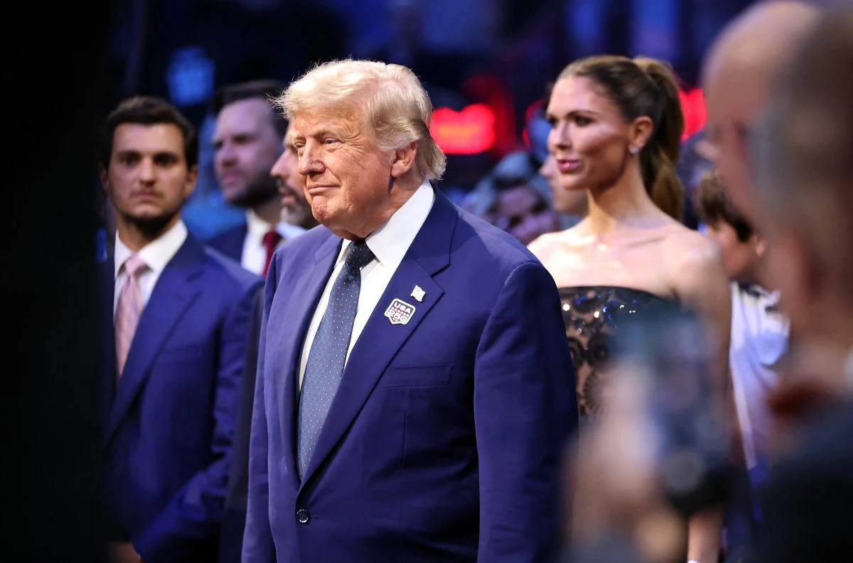 Mężczyzna w eleganckim granatowym garniturze z białą koszulą i krawatem stoi w centrum sceny, otoczony przez innych formalnie ubranych ludzi w tłumie o stonowanym tle.