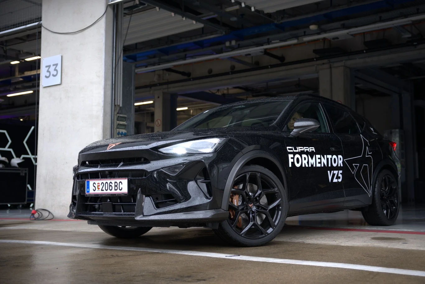 Mimo debiutu w 2020 r., zeszły rok Formentor zakończył jako najlepiej sprzedające się auto w gamie Cupry - odpowiadał za prawie 1/3 globalnej sprzedaży. Czarny samochód Cupra Formentor VZ5 z białymi napisami na drzwiach, stojący na mokrym betonie przy otwartym garażu z numerem 33.