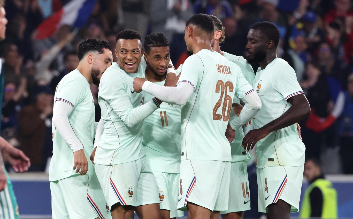 Kylian Mbaape wraz z piłkarzami reprezentacji Francji Kylian Mbappé i piłkarze Francji w jasnych strojach podczas meczu, otoczeni kibicami na stadionie.