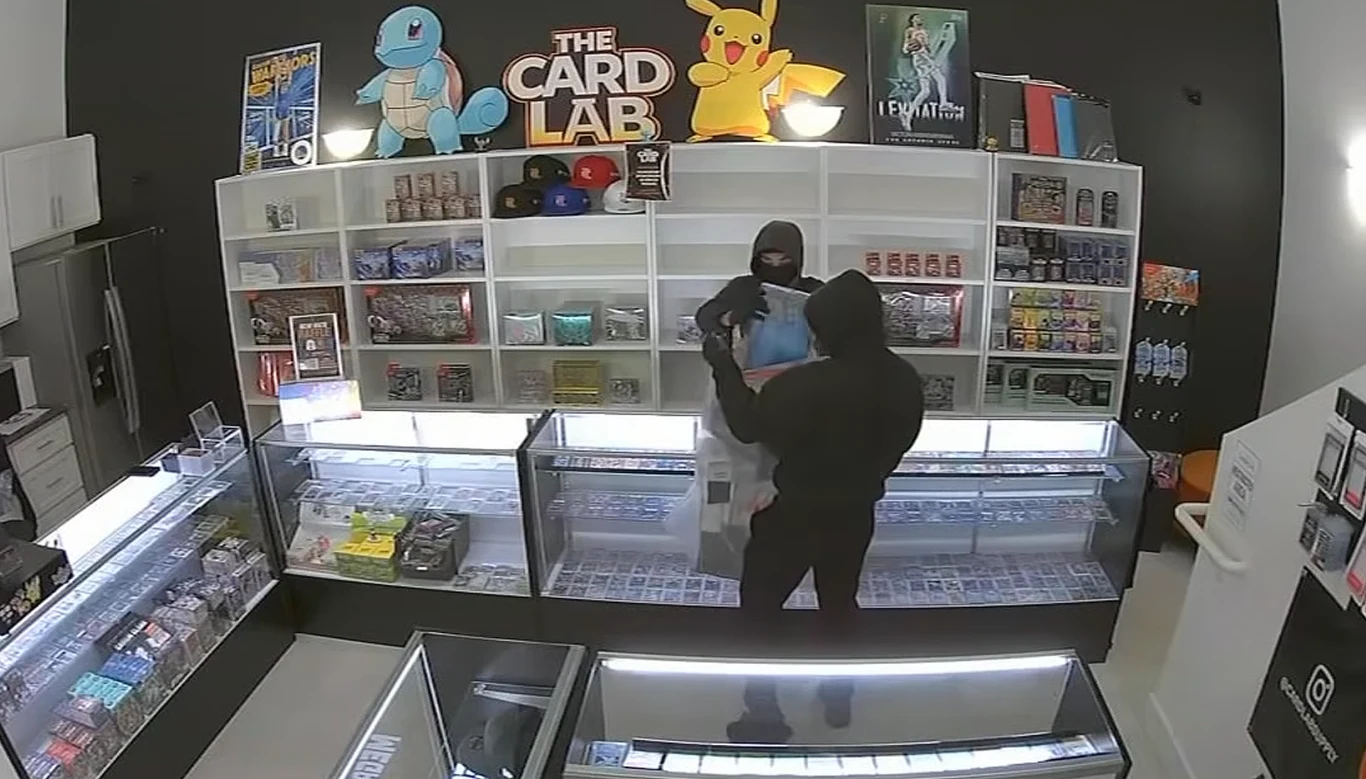 źródło: ABC7 Dwóch zamaskowanych mężczyzn w czerni w sklepie, jeden trzyma pudełko z kartami kolekcjonerskimi Pokémon.