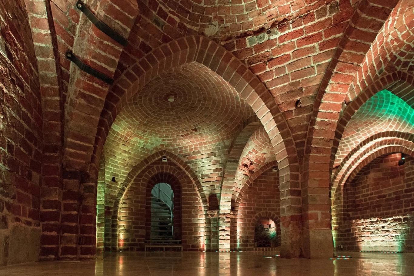 Gotyckie sklepienia krzyżowo-żebrowe z czerwonej cegły, masywne filary i miękkie oświetlenie podkreślające architektoniczne detale zabytkowej piwnicy.