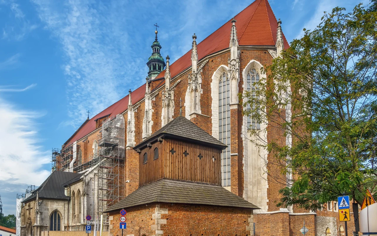 Kościół świętej Katarzyny Aleksandryjskiej i świętej Małgorzaty w Krakowie Gotycki kościół w Krakowie, z czerwonym dachem i wysokimi oknami, obok którego stoi drewniana dzwonnica.