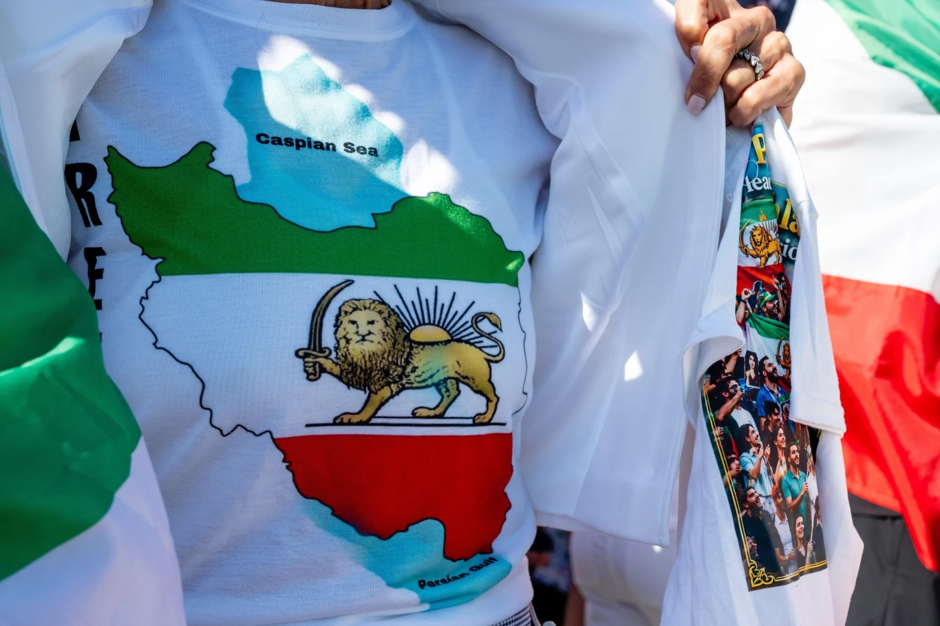 Zakazany symbol przez irański reżim Mapa Iranu z herbem przedstawiającym lwa z mieczem i słońcem na tle kolorów flagi, nadrukowana na białej koszulce.