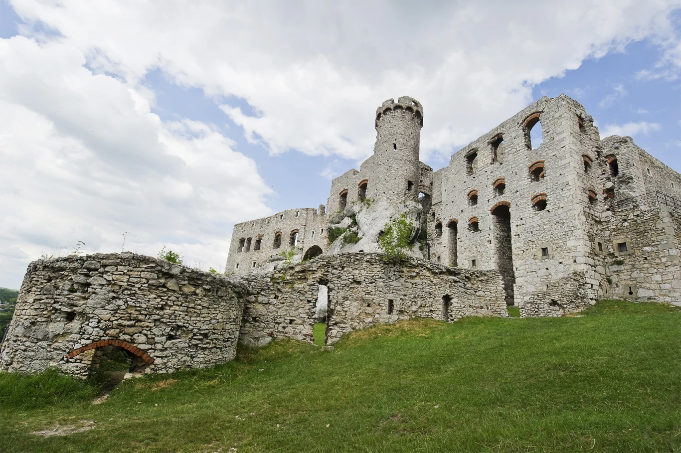 To jeden z najpiękniejszych zamków w Polsce. Z Krakowa dojedziesz do niego w nieco ponad godzinę. Ruiny Zamku Ogrodzieniec z kamiennymi murami i okrągłą wieżą na zielonym wzgórzu.