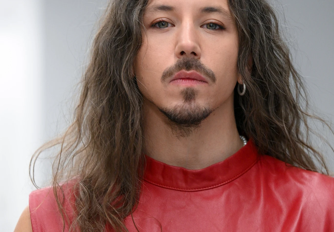 Michał Szpak Michał Szpak z długimi, falowanymi włosami, w czerwonym topie z imitacji skóry, z kolczykiem w lewym uchu.