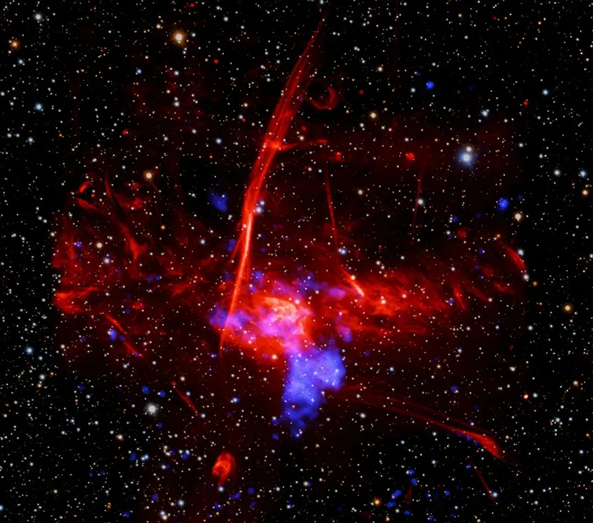 Sagittarius C - miejsce w pobliżu supermasywnej dziury Drogi Mlecznej, gdzie wykryto pozostałości supernowej. Jasne, nieregularne chmury gazu w kolorach czerwonym i fioletowym kontrastujące z czarnym tłem wszechświata, wypełnionym licznymi, drobnymi gwiazdami.