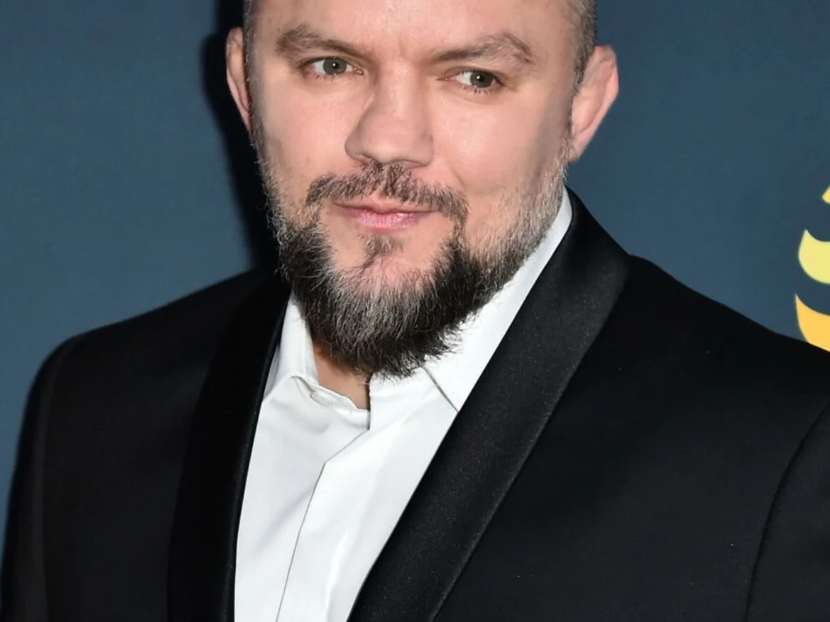 Juras Łukasz Jurkowski w eleganckiej stylizacji na ciemnym tle z grafiką.