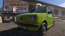 Zielony fiat 126p z kozłem leżącym na jego dachu, ustawiony przed budynkiem z reklamą sklepu motoryzacyjnego.