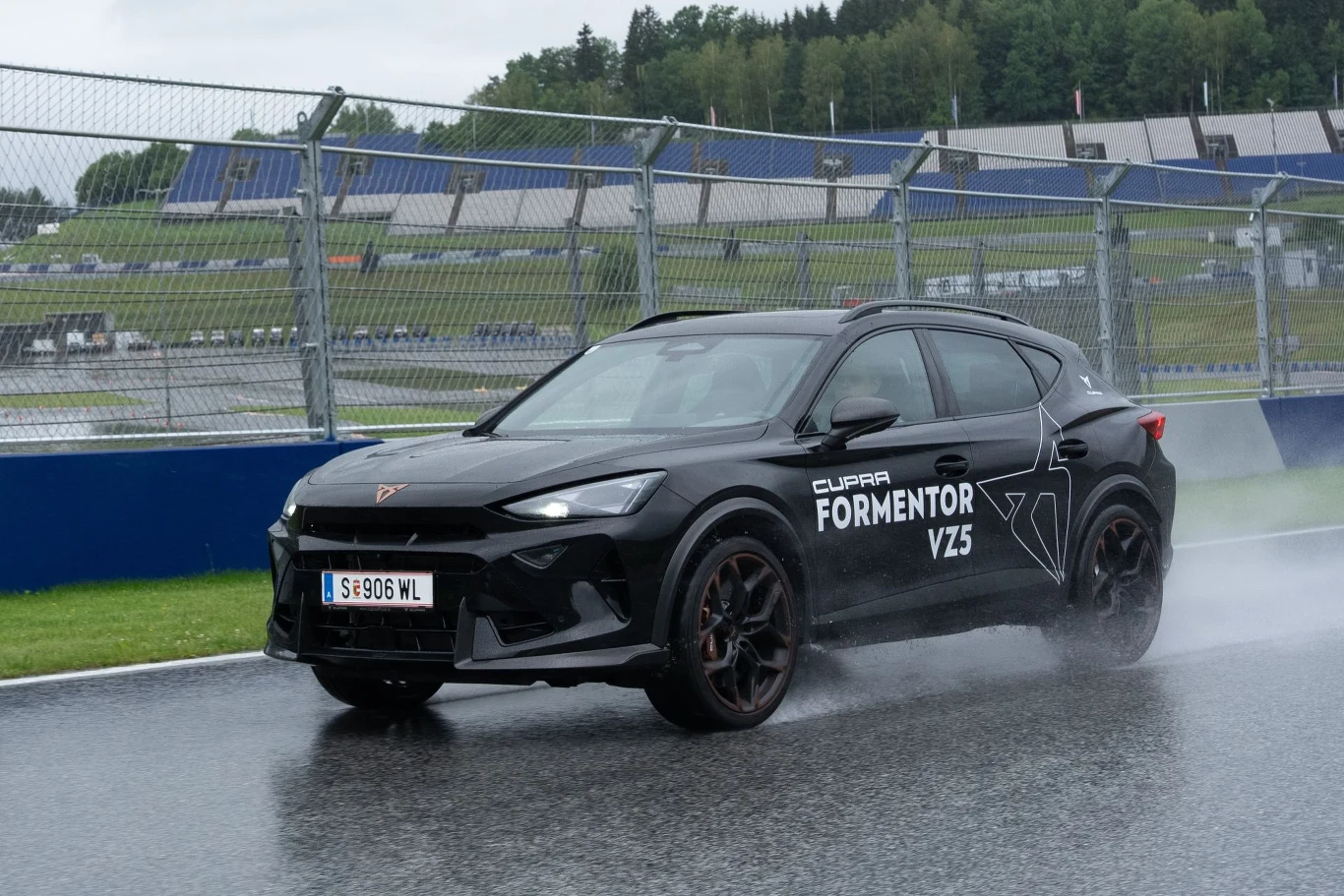 Czarny samochód Cupra Formentor VZ5 z przyciemnianymi szybami dynamicznie pokonuje zakręt na mokrym torze wyścigowym, wzbijając wodę spod kół.