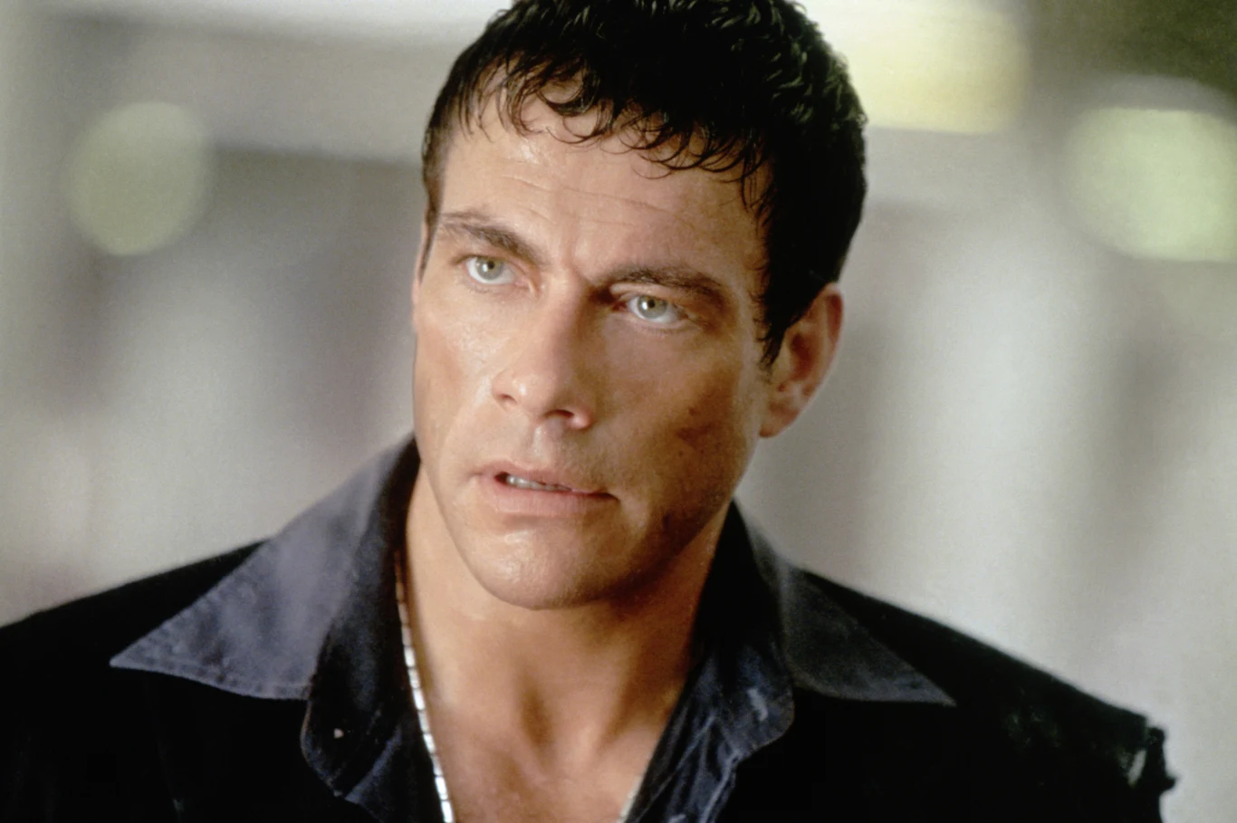 Jean-Claude Van Damme w filmie "Za ciosem" Jean-Claude Van Damme w filmie "Za ciosem". Krótkie ciemne włosy, niebieskie oczy, ciemna koszula i marynarka.