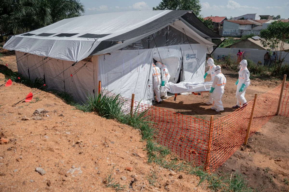 Epidemia wirusa Ebola w Kongo. Zdjęcie ilustracyjne Czterech pracowników w kombinezonach przenosi ciało na noszach do białego namiotu medycznego w Kongo.