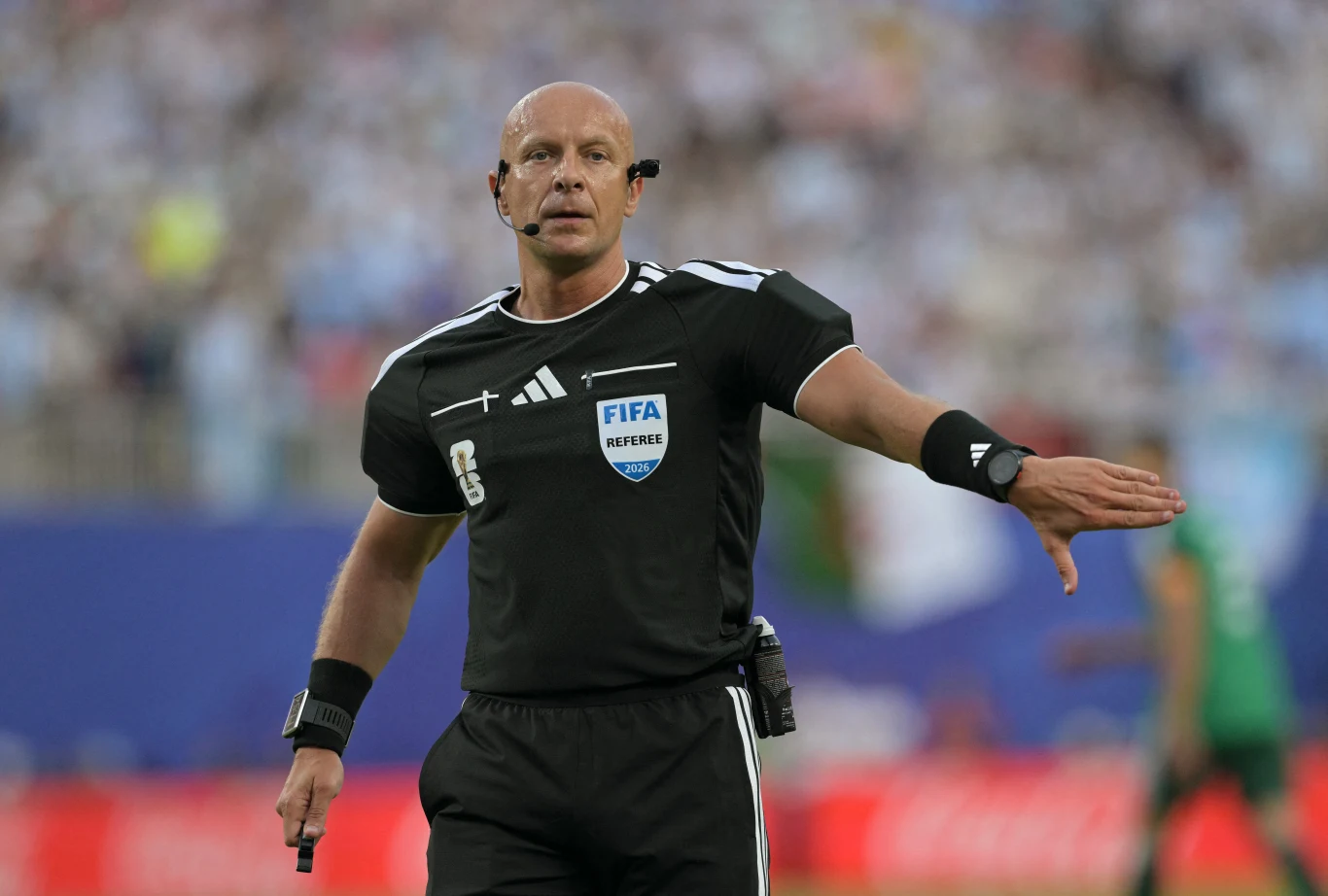 Szymon Marciniak znów w gronie najlepszych sędziów prowadzi mecze na mistrzostwach świata Sędzia piłkarski w czarnej koszulce FIFA wydaje decyzję podczas meczu, mając uniesione jedno ramię i trzymając gwizdek w dłoni.