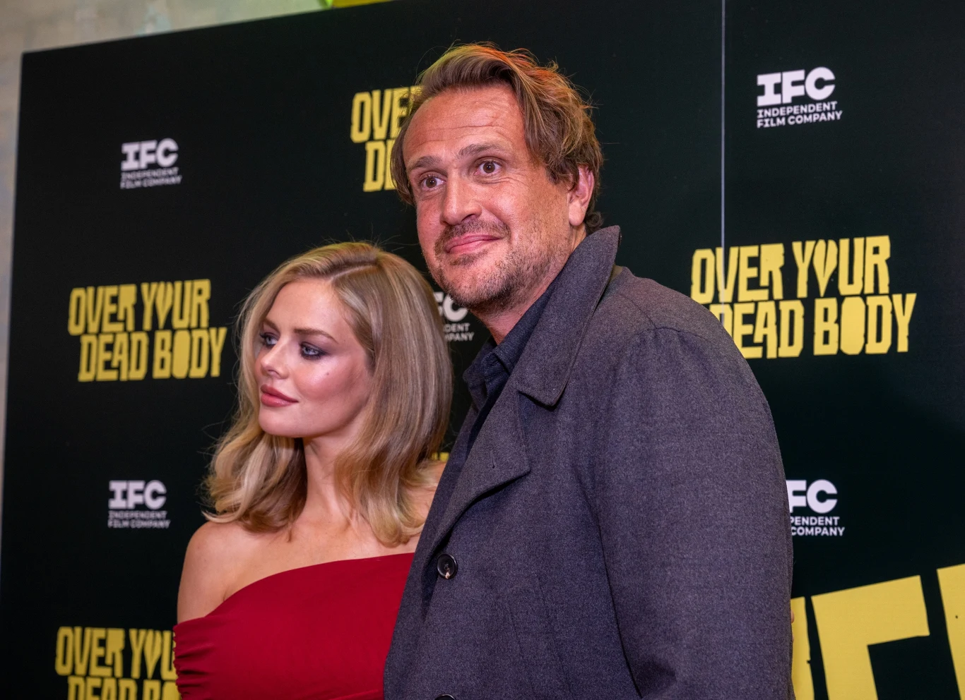 Kobieta w czerwonej sukience i mężczyzna w szarym płaszczu pozują razem na tle ścianki z napisem 'Over Your Dead Body' oraz logo IFC.