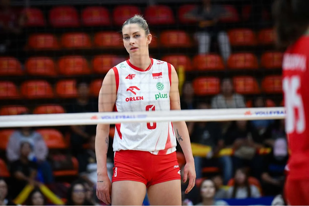 Zawodniczka polskiej reprezentacji siatkówki w biało-czerwonym stroju sportowym stoi na boisku, skoncentrowana przed siatką podczas meczu.