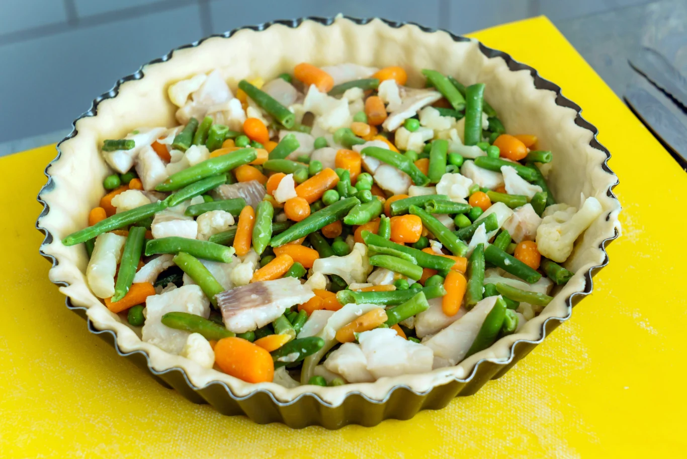 quiche tart Tarta z kruchego ciasta w formie, wypełniona mrożonymi warzywami: fasolką, marchewką, groszkiem i kalafiorem.