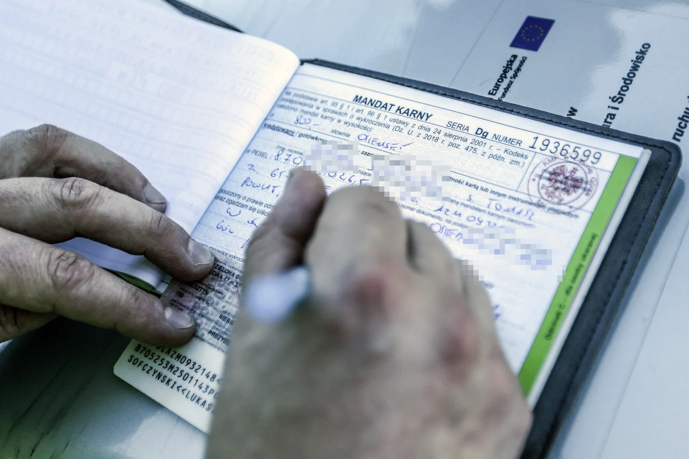 Handel punktami karnymi to nadal często spotykany proceder Ręka osoby wypełniającej formularz mandatu karnego z widocznymi danymi oraz pieczątką urzędową.