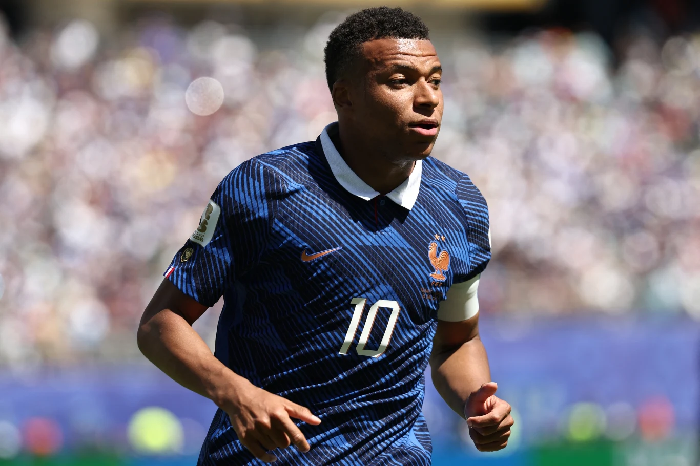 Kylian Mbappe Kylian Mbappe w niebieskiej koszulce z numerem 10 i opaską na ramieniu biegnie po boisku podczas meczu.