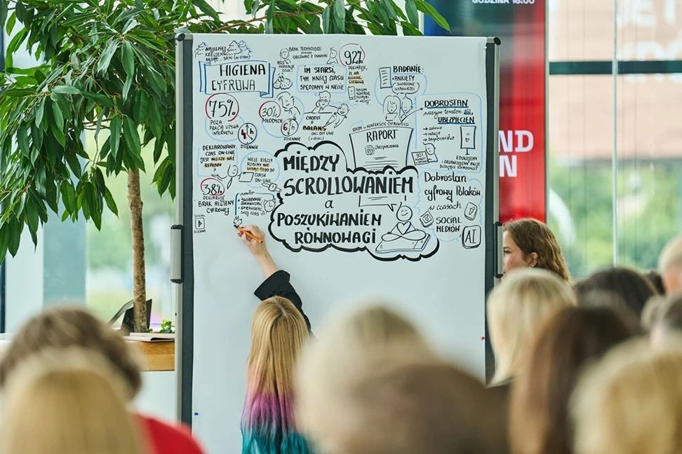 Kobieta rysuje na dużej tablicy ilustrowany notatnik z napisem „Między scrollowaniem a poszukiwaniem równowagi”, wokół której znajdują się grafiki i hasła dotyczące higieny cyfrowej, problemów scrollowania oraz rekomendacji działań, a z przodu obserwuj...