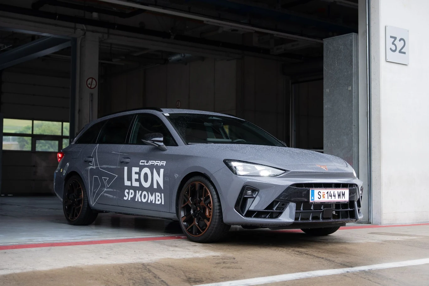 Sportowe kombi CUPRA Leon SP w matowym, szarym kolorze, widoczne w nowoczesnym garażu przy torze, wyróżniające się agresywnym designem przodu oraz dużymi felgami o miedzianym wykończeniu.