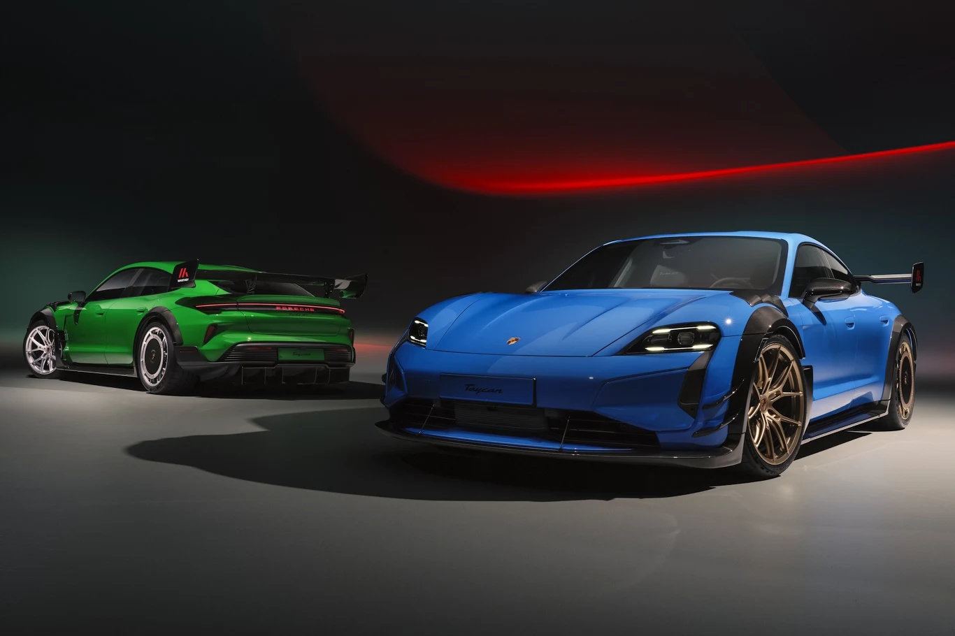 Dwa sportowe samochody Porsche w intensywnych kolorach – zielony w tle i niebieski na pierwszym planie, oba z aerodynamicznymi dodatkami i charakterystycznym designem marki.