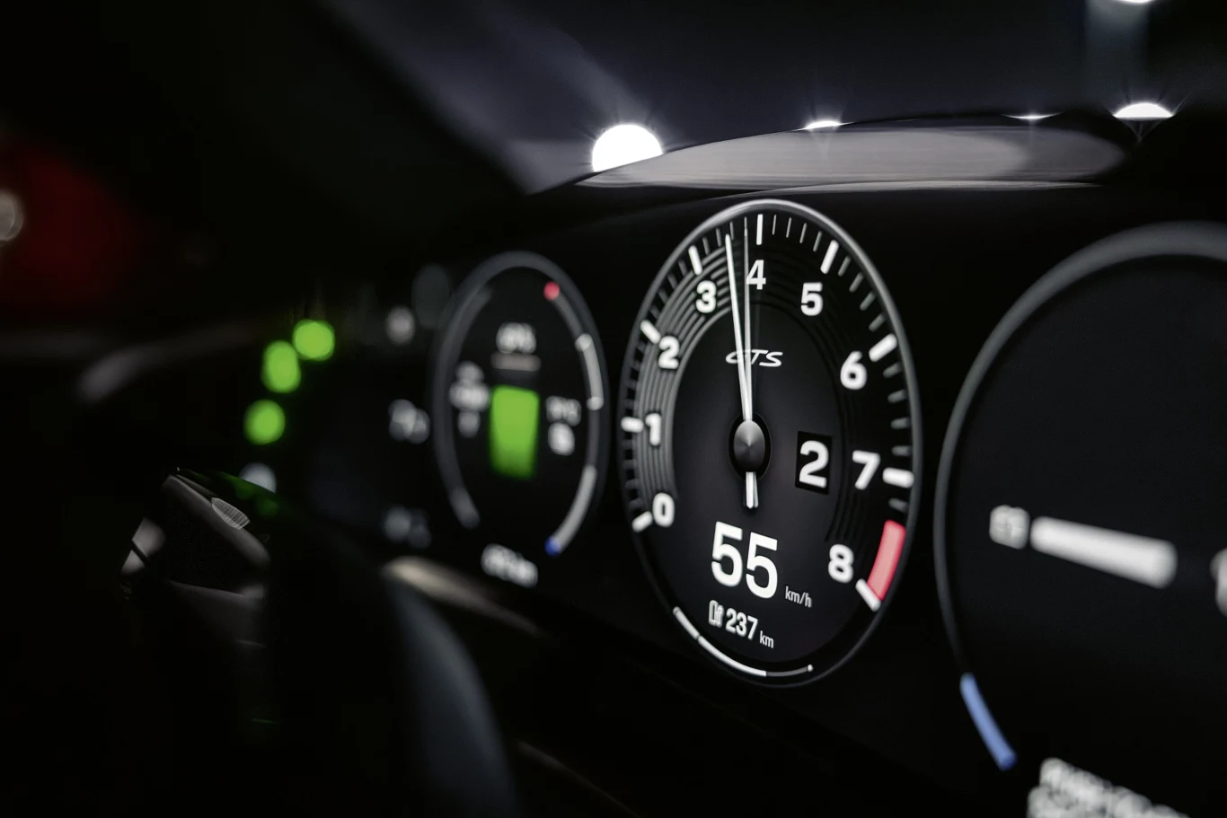 Kokpit samochodu sportowego z wyraźnie widocznym prędkościomierzem wskazującym 55 km/h oraz obrotomierzem, cyfrowe wskaźniki i oświetlone kontrolki na desce rozdzielczej.
