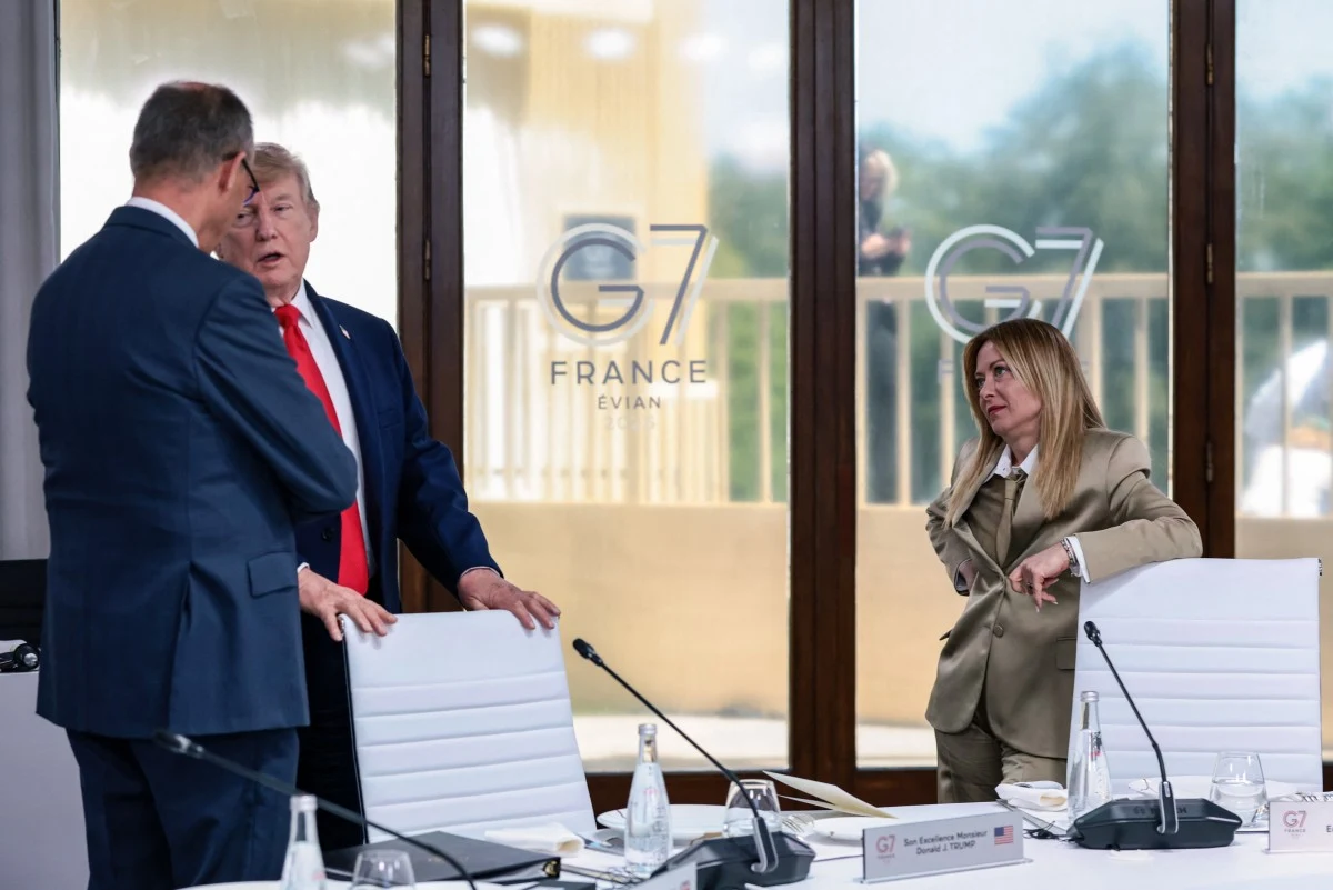Friedrich Merz rozmawia z Donaldem Trumpem i Giorgią Meloni Trzech elegancko ubranych uczestników rozmowy w nowoczesnej sali konferencyjnej z dużymi oknami, na których widnieje logo szczytu G7 France Evian; na stole stoją butelki z wodą, szklanki i materiały konferencyjne.