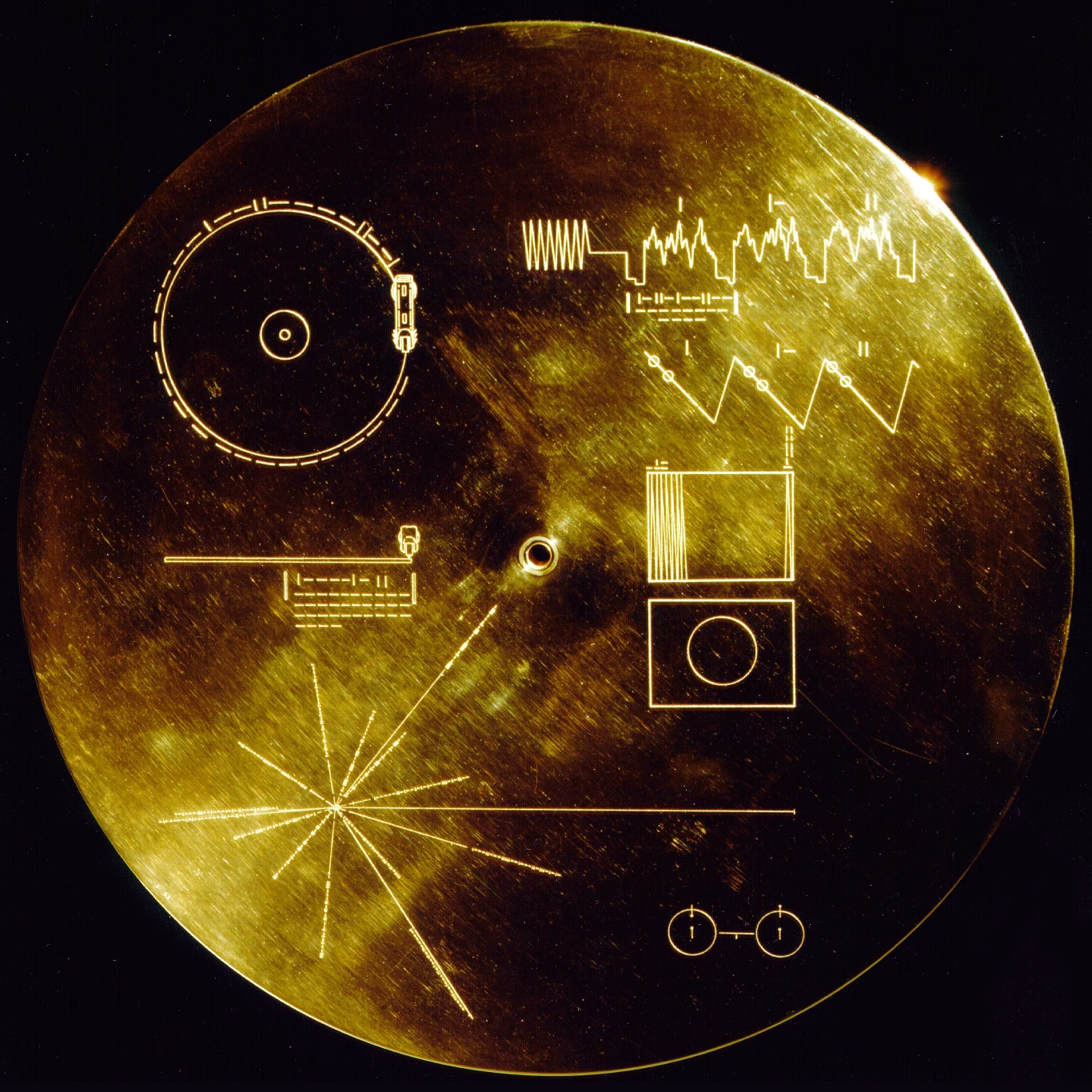 Złota płyta z wygrawerowanymi symetrycznymi wzorami, schematami technicznymi i symbolami, w tym diagram przedstawiający odtwarzacz, fale dźwiękowe oraz schematy atomów i układu słonecznego.