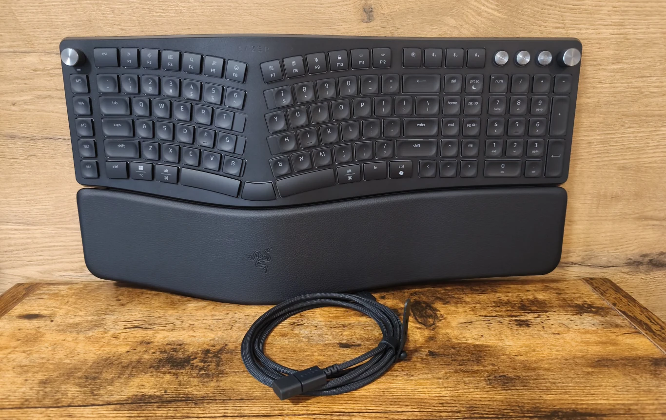 Ergonomiczna, podzielona klawiatura z podkładką pod nadgarstki oraz dołączonym przewodem USB, całość na drewnianym blacie.