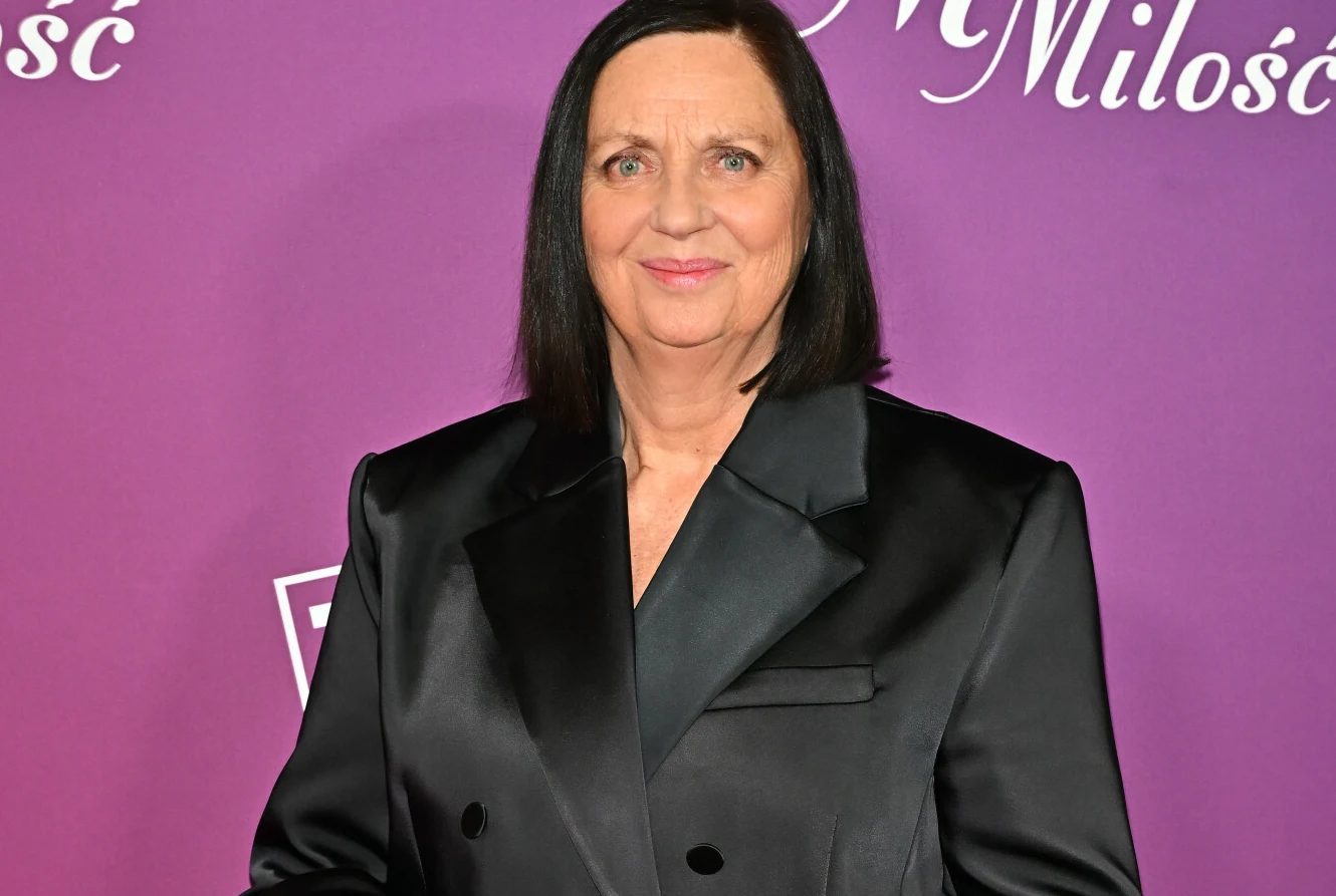 Hanna Mikuć Hanna Mikuć w czarnej marynarce pozująca na tle fioletowej ścianki z napisami.