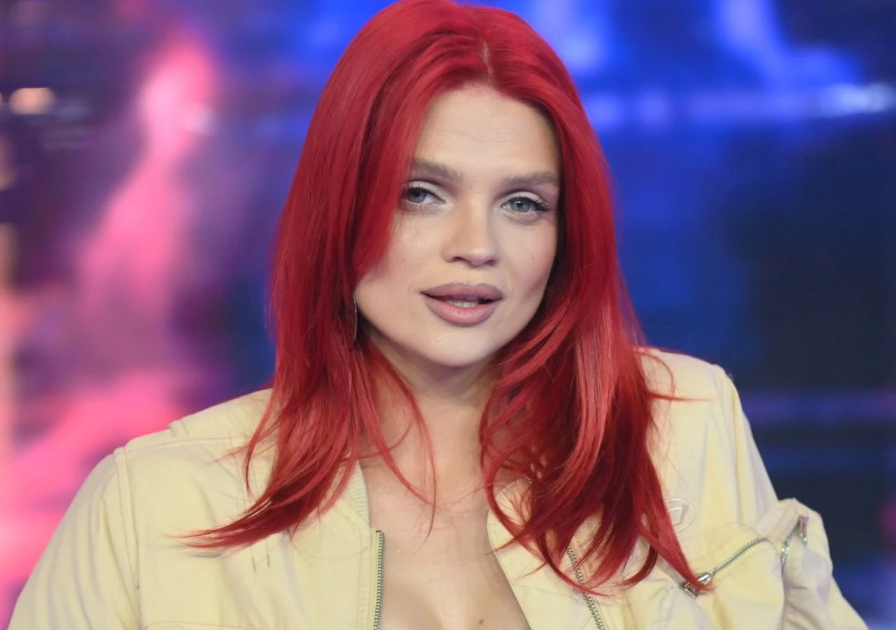 Margaret Piosenkarka Margaret z czerwonymi włosami w jasnej kurtce na tle kolorowego oświetlenia