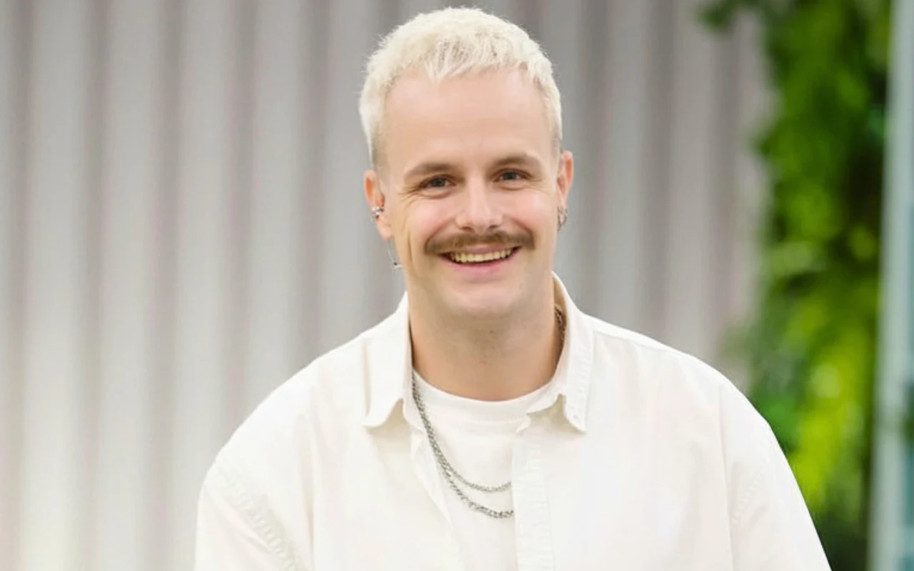 Filip Mettler w "halo tu polsat" Uśmiechnięty Filip Mettler w białej koszuli w studiu "halo tu polsat"