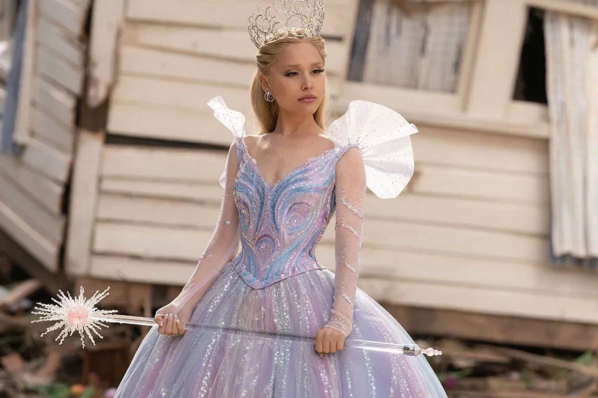 Ariana Grande w scenie z filmu "Wicked: Na dobre" Ariana Grande jako Glinda w filmie "Wicked: Na dobre" w ozdobnej sukni i tiarze, z różdżką, na tle ruin.