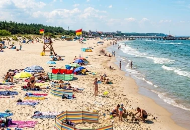 Słoneczna plaża nad Bałtykiem latem — kolorowe parasole plażowe, parawany i wieża ratownika, w tle molo