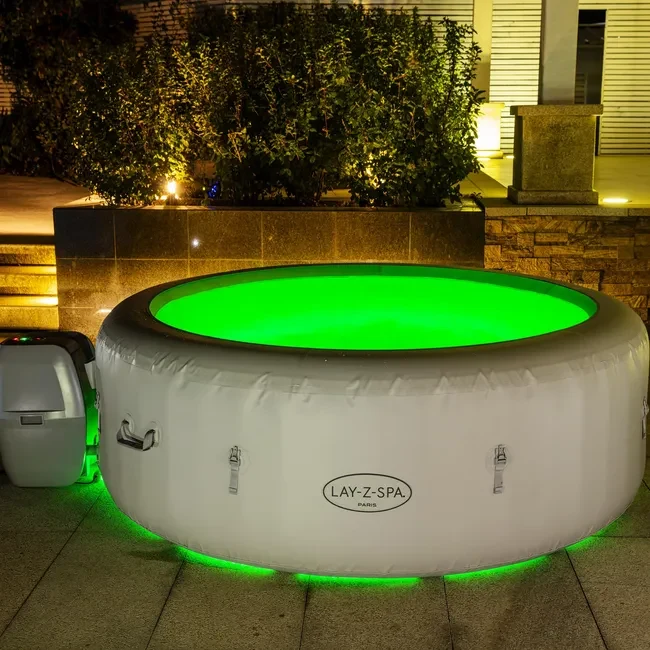 Nadmuchiwane jacuzzi z podświetleniem LED w intensywnym zielonym kolorze ustawione na zewnątrz przy ścianie z roślinnością w tle.